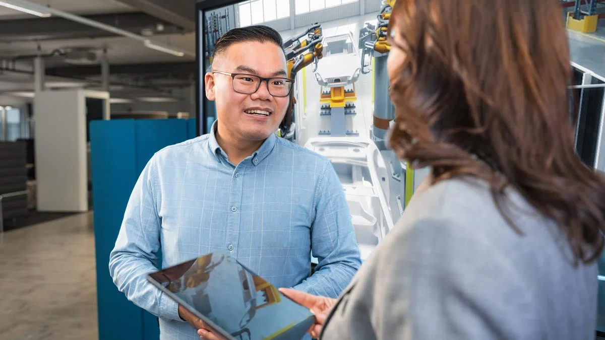 Im Büro unterhalten sich ein Mann und eine Frau mit einem Tablet in der Hand über die innovativen Dienstleistungen von Volkswagen Group Services.